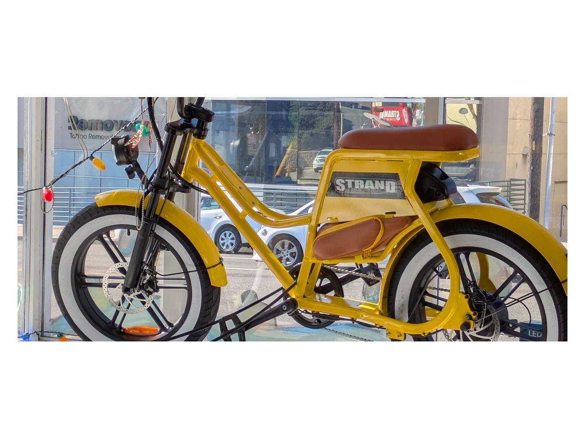 A Strand moto-style e-bike in red, parked against greenery.
